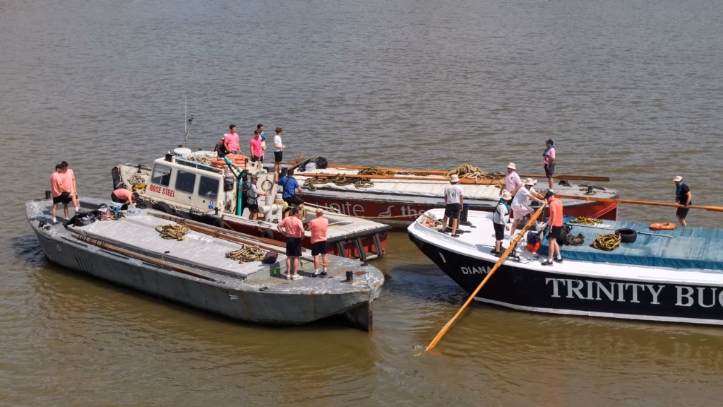 Crews aboard the Trinity Buoy Wharf barge before the start of the Thames barge driving race, an oar run out over the side