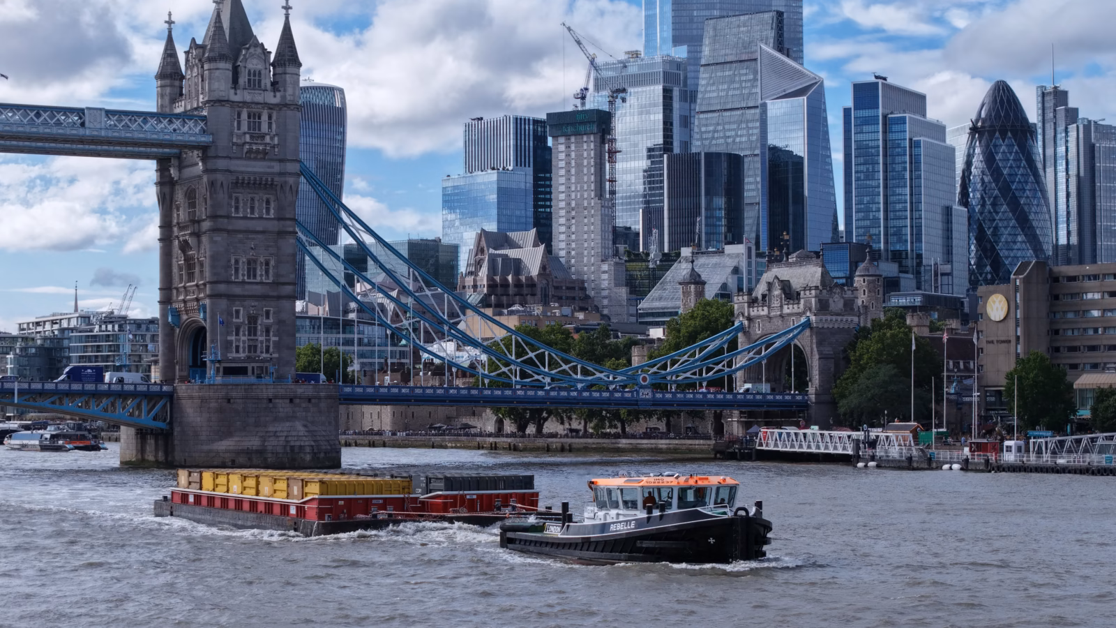 A Cory container barge under tow passing Tower Bridge with the City of London skyline behind
