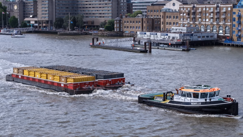 The Cory tug Rebelle towing the container barge Gemma D on the River Thames, tow line taut and the loaded containers astern