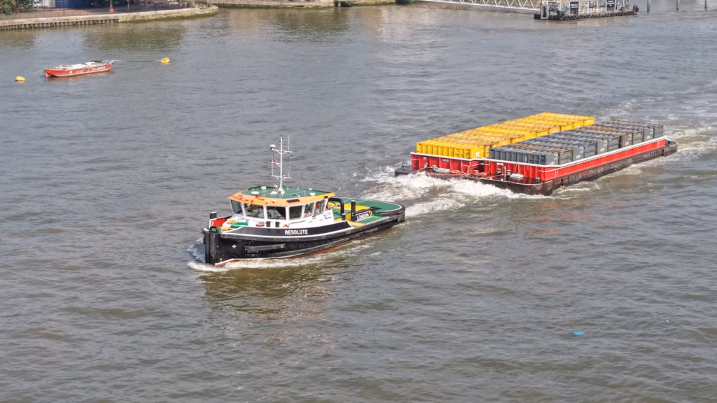 Cory tug Resolute towing a loaded container barge up the Thames, captured by drone