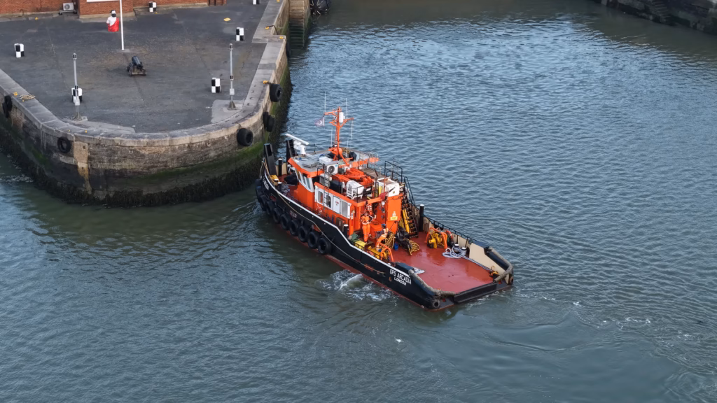 Overhead aerial photograph of a tug held against the dockyard wall at Chatham while crew transfer ashore