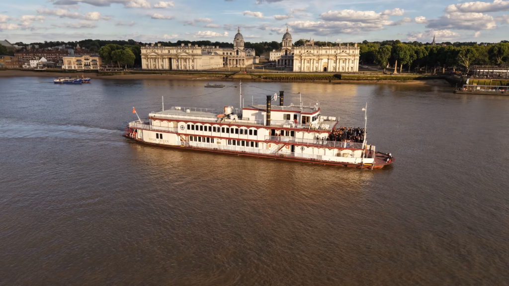 The paddle steamer Dixie Queen passing the Old Royal Naval College at Greenwich in evening light, with guests on the stern deck