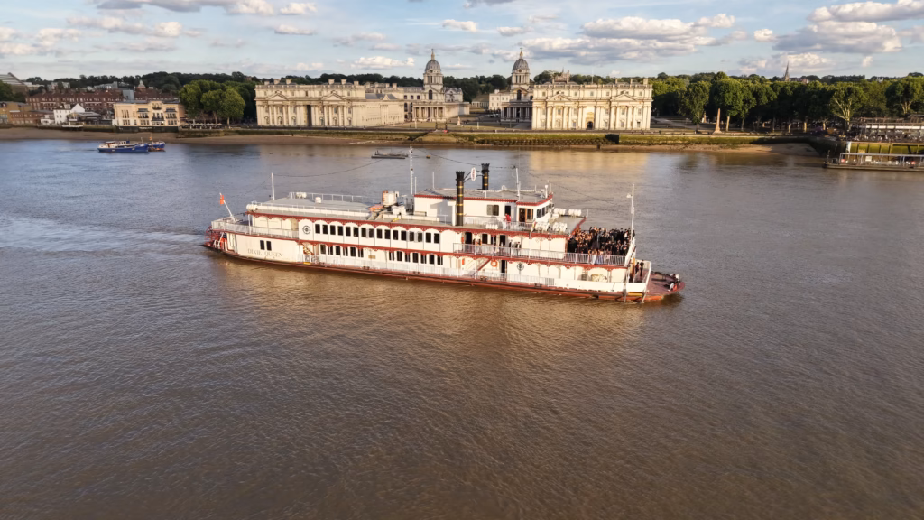 Aerial view of the Dixie Queen under way on the tidal Thames at Greenwich in low evening sun