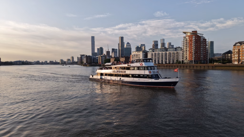 The Dutch Master on the tidal Thames in low evening light with the Canary Wharf towers on the skyline behind