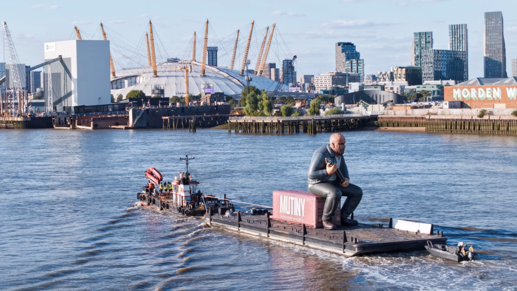 Mutiny: Jason Statham Brand Activation on the Thames 7 Aerial view of the inflatable Jason Statham seated on the pink Mutiny shipping container aboard a flat-top pontoon under tow on the River Thames