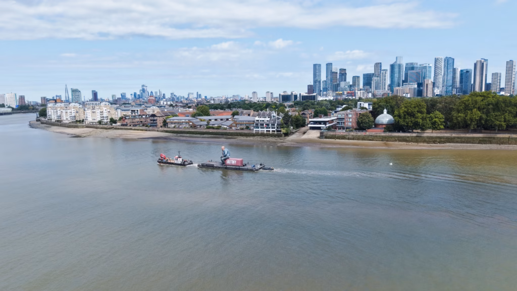 Mutiny: Jason Statham Brand Activation on the Thames 5 Evening aerial photograph of the giant inflatable Jason Statham on the Mutiny container passing the Greenwich Peninsula, with the O2 arena behind