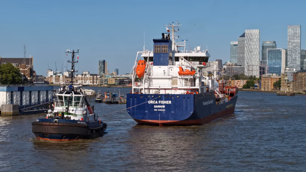 Aerial view of the Orca Fisher tanker under tug escort on the tidal River Thames, London