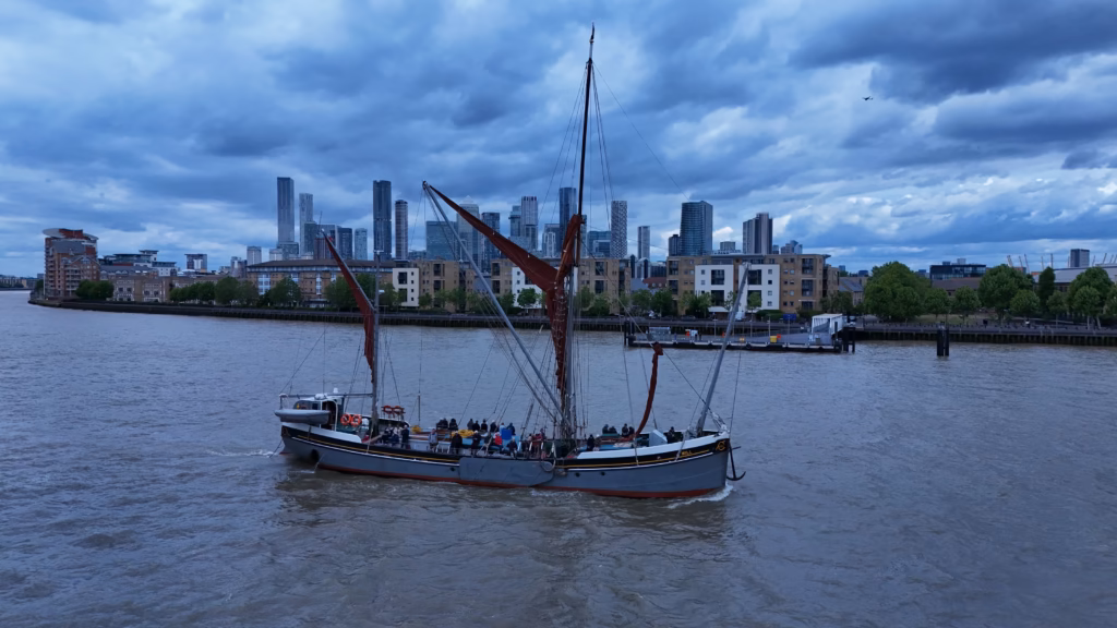 Aerial view of the sailing barge Will on the River Thames in London, tan sails brailed and passengers aboard