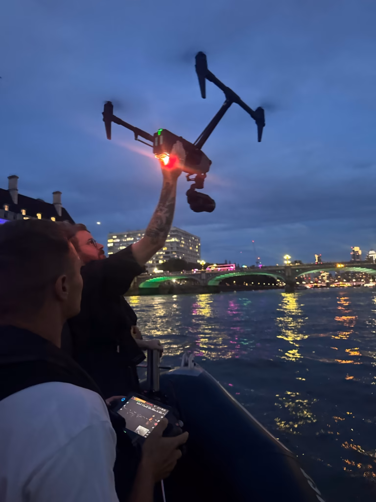 Drone crew on our RIB catching a cinema drone by hand after dark, with Westminster Bridge and County Hall lit up behind