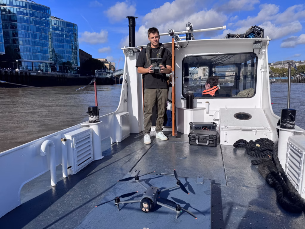 Drone on a hatch on the aft deck of a boat in the Pool of London, the pilot standing by the wheelhouse