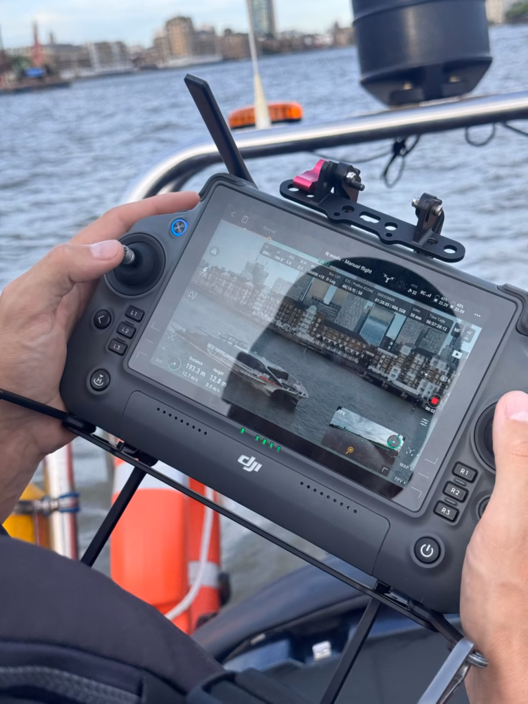 Drone pilot on our RIB holding the controller, the live feed from the drone on its screen and the river behind