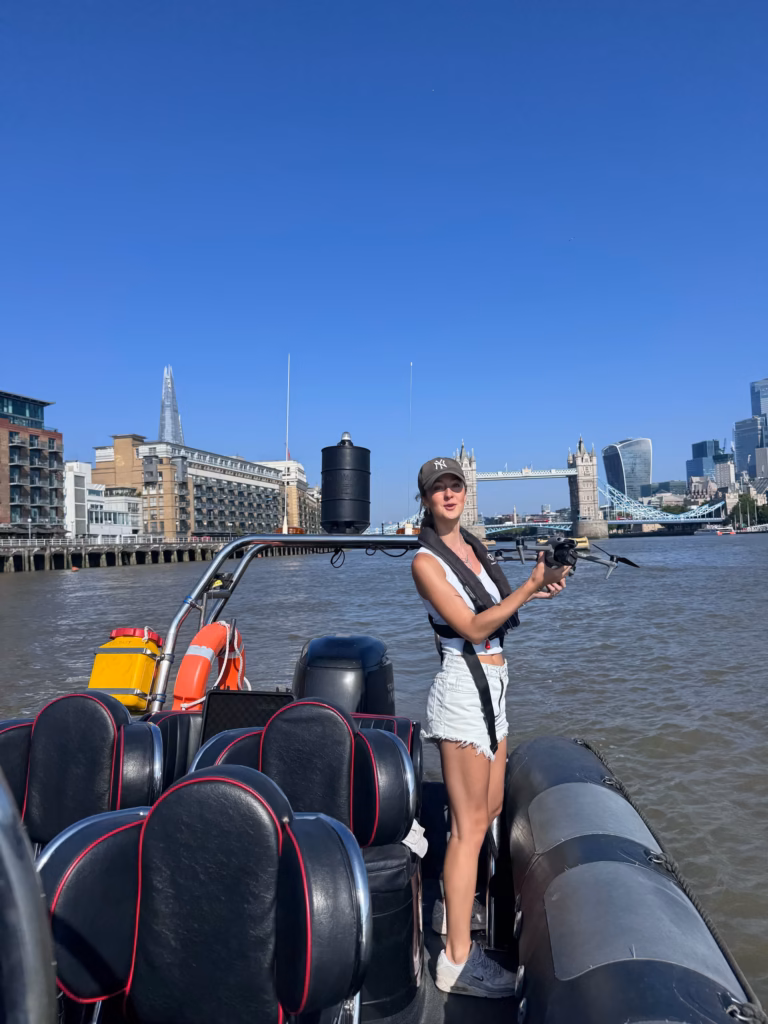 Drone operator standing in our RIB on the Thames with her drone, the Shard and Tower Bridge behind