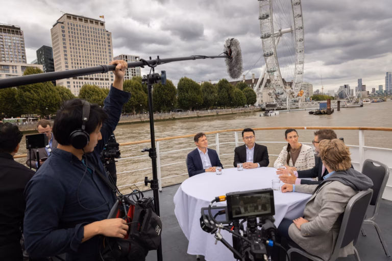 Boom operator and camera crew filming a roundtable on the Thames, with the London Eye behind