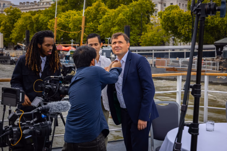 Crew fitting a radio mic to a contributor on deck before filming on the Thames